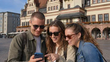 Three people smiling at a phone outdoors.