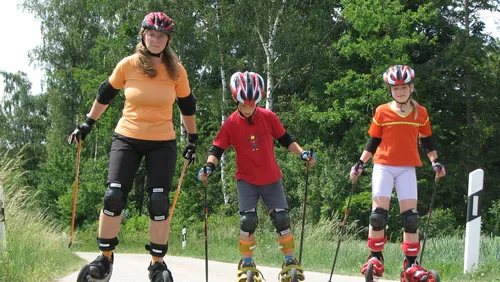 Drei Personen beim Rollerskifahren auf einem Weg.