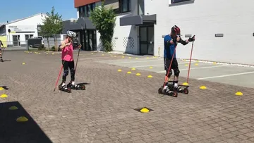 Two people roller skiing outdoors on pavement.