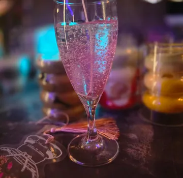 Sektglas mit sprudelndem Getränk in dunkler Bar.