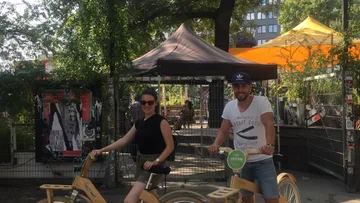 Two people riding bicycles, outdoor market background.