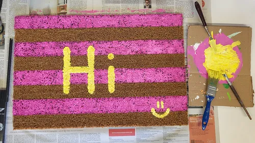 Doormat painted with pink stripes and 'Hi'.