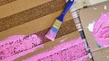 Pinsel trägt rosa Farbe auf Karton auf.