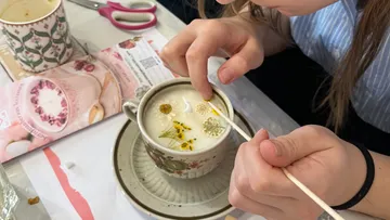 Person verziert Kerze mit getrockneten Blumen.