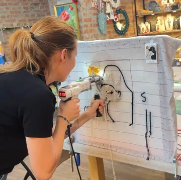 Woman using tufting gun on fabric canvas.