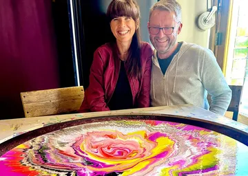Two people smiling near colorful artwork.