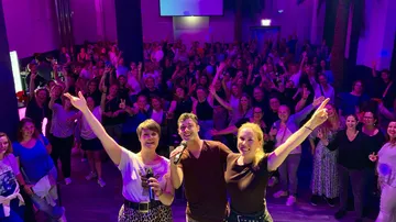 Three people posing, joyful crowd behind