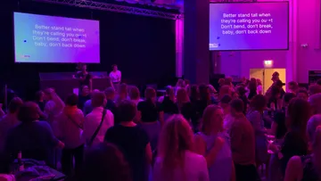 Menschenmenge singt Karaoke in schwach beleuchtetem Raum.