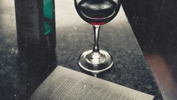 Weinglas auf Tisch neben offenem Buch.