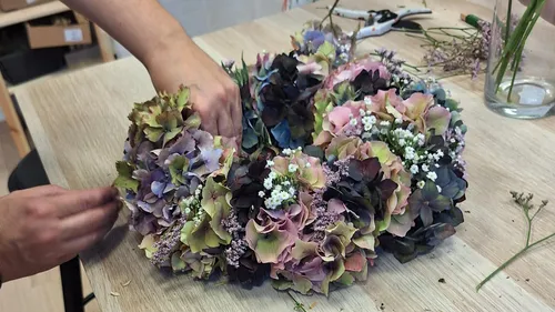 Person assembling hydrangea wreath on table.