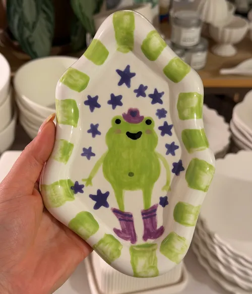 Hand hält Froschschale mit Sternen, Pflanzen im Hintergrund.