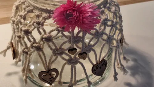 Glass jar with macramé cover and pink flower.