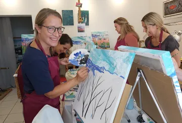 Women painting on canvases in art studio.