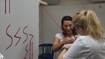 Zwei Frauen weben Fäden an Textilrahmen.