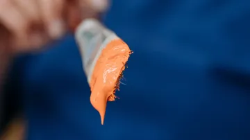 Paintbrush holding orange paint, blue background.