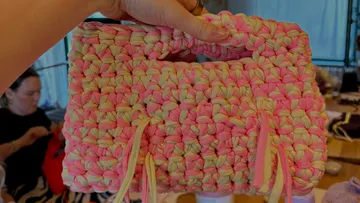 Hand hält eine bunte gestrickte Tasche drinnen.