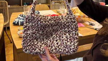 Hand holding knitted bag over table.