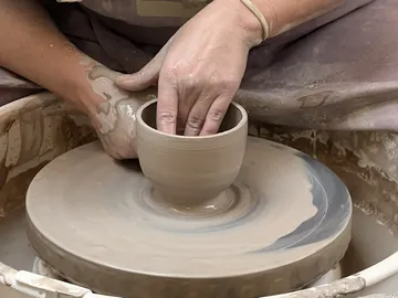Potter shaping clay bowl on spinning wheel.