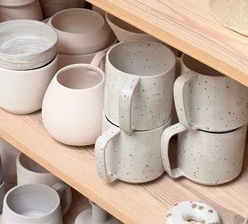 Keramikbecher und Schalen auf Holzregalen.