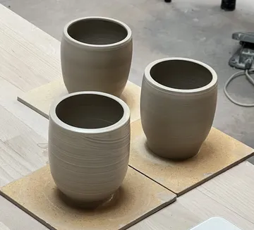 Drei Tontöpfe trocknen auf Holzplatten.