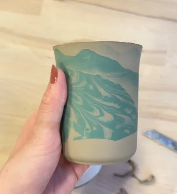 Hand hält verzierten Keramikbecher, Holztisch.