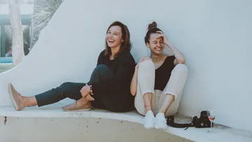 Two women laughing seated outdoors.
