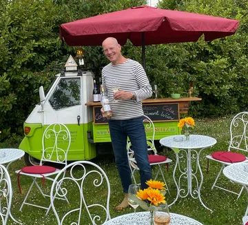 Man holding wine bottle outdoors near cart.