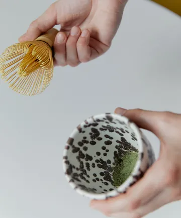 Hände halten Matcha-Besen und Schale.