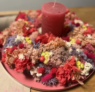 Red candle surrounded by colorful dried flowers.