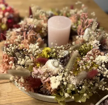 Candle surrounded by dried flowers on table.