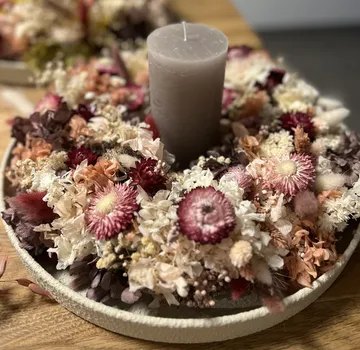 Kerze von Trockenblumen auf Tisch umgeben.