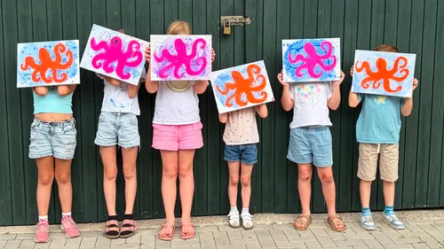 Kids hold octopus paintings against a wall.