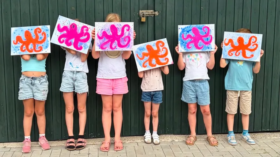 Children holding octopus paintings on green wall.