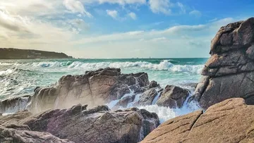 Felsige Küste mit brechenden Wellen, bewölkter Himmel.