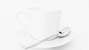 Weiße Tasse und Untertasse mit Löffel auf Tisch.