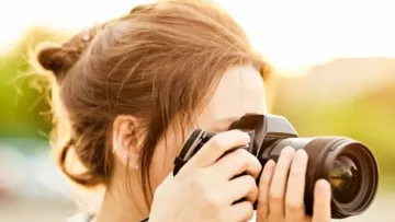 Frau fotografiert draußen, sonniger Hintergrund.