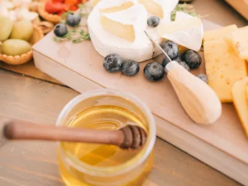 Cheese and fruit on a table with a honey jar.