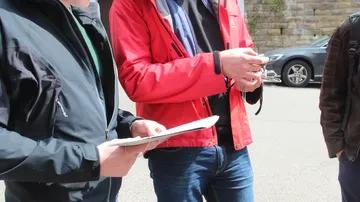 Drei Personen diskutieren draußen mit Tablet.