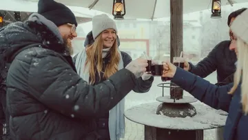 Gruppe stößt mit warmen Getränken im Schnee an.
