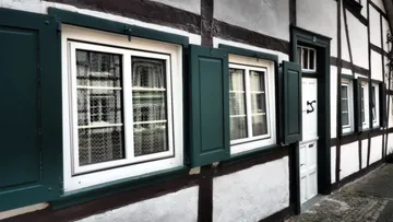 Grüne Fensterläden an weißem Fachwerkhaus.