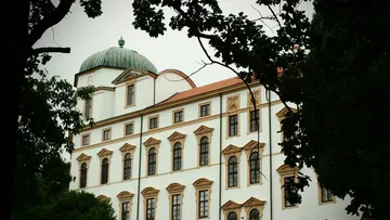 Historisches Gebäude mit Kuppel, von Bäumen umgeben.