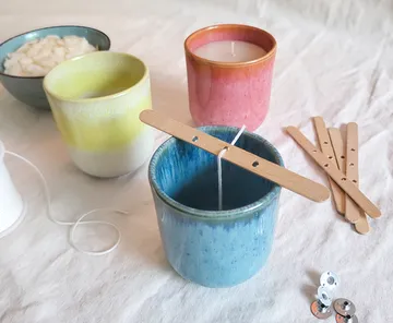 Colorful candles in ceramic cups, wooden sticks.