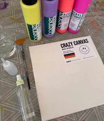 Leinwand und Farben auf gemustertem Tisch.