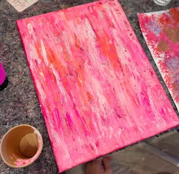 Leinwand mit pink-orange Abstraktmalerei auf Tisch.