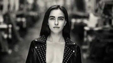 Woman in studded jacket stands outdoors.