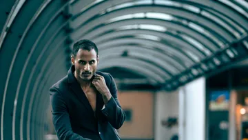Man posing in arched urban corridor.