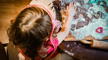 Child rolling dough with cookie cutters nearby.