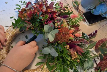 Hände arrangieren Blumenkranz auf einem Tisch.