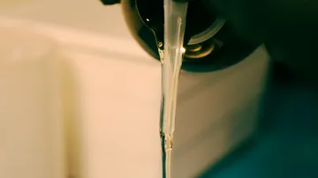 Flüssigkeit gießt aus Flasche in dunklem Umfeld.