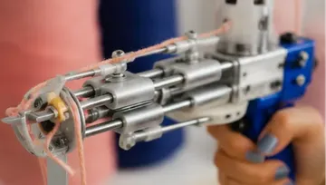 Tufting gun held, threads extending, blurred background.